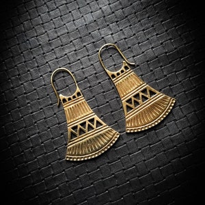 May include: A pair of gold-toned earrings with a geometric design. The earrings are shaped like a triangle with a rounded bottom and have a repeating pattern of triangles and lines.