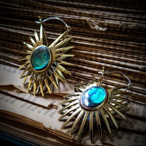 May include: A pair of gold-toned earrings with a sunburst design and a turquoise gemstone in the center of each earring.