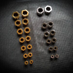 Peut inclure: Un ensemble de jauges d'oreille hexagonales dorées et argentées de différentes tailles. Les jauges sont disposées en deux colonnes, les plus grandes en haut et les plus petites en bas.