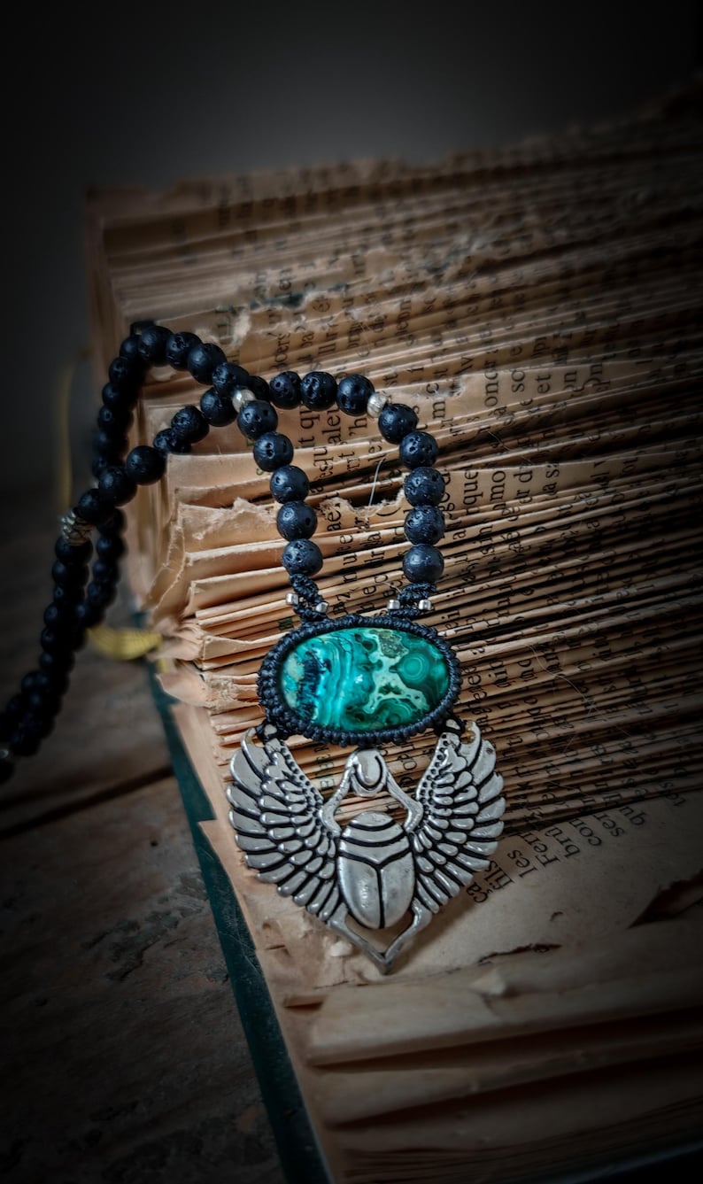 May include: A black lava rock beaded necklace with a silver scarab beetle pendant. The pendant features a green stone with a marbled pattern.