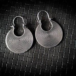 Peut inclure: Une paire de boucles d'oreilles créoles en argent avec un motif en spirale. Les boucles d'oreilles sont sur un fond texturé noir.