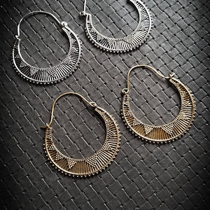 Könnte beinhalten: Vier Creolen, zwei silberne und zwei goldene, mit geometrischem Muster. Die Ohrringe liegen auf einer schwarzen, strukturierten Oberfläche.