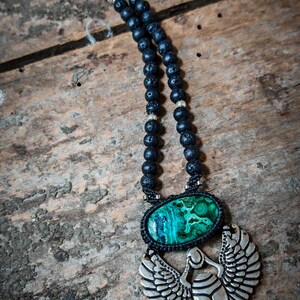 May include: A black lava rock beaded necklace with a silver scarab beetle pendant. The pendant features a green malachite stone.
