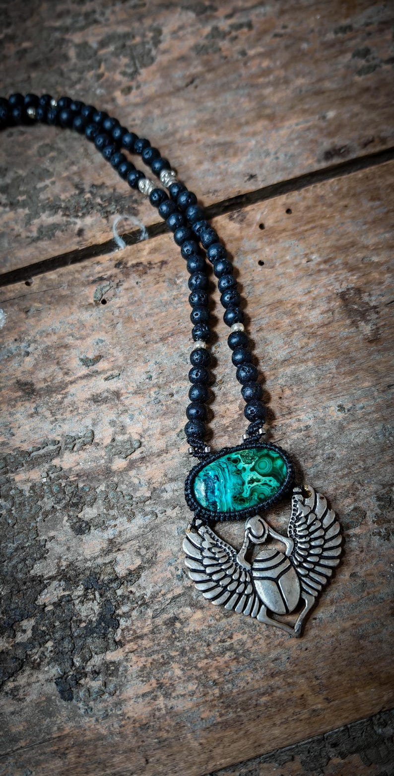 May include: A black lava rock beaded necklace with a silver scarab beetle pendant. The pendant features a green malachite stone.