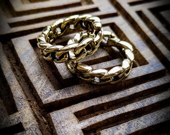 以下が含まれることがあります： 幾何学模様の木製表面に置かれた、2つの金色のチェーンリンクリング