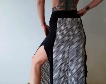 Pode incluir: Uma saia maxi preta com uma fenda lateral e um padrão geométrico branco e preto no lado direito. A saia é usada com botas marrons.