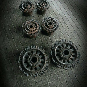 Può includere: Set di sei dilatatori per orecchie in legno con intricati disegni intagliati. I dilatatori sono di colore marrone scuro e hanno una forma circolare con un foro centrale.