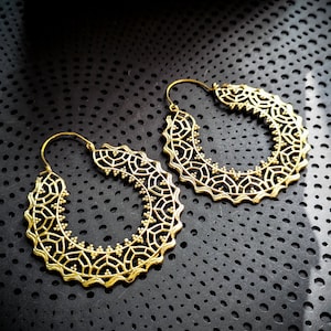Peut inclure: Une paire de boucles d'oreilles créoles dorées avec un design délicat et complexe. Les boucles d'oreilles sont en métal et ont une forme circulaire.