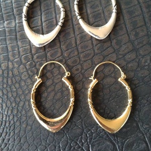 May include: Two pairs of hoop earrings, one pair is silver and the other is gold. Both pairs have a unique, slightly pointed, teardrop shape.