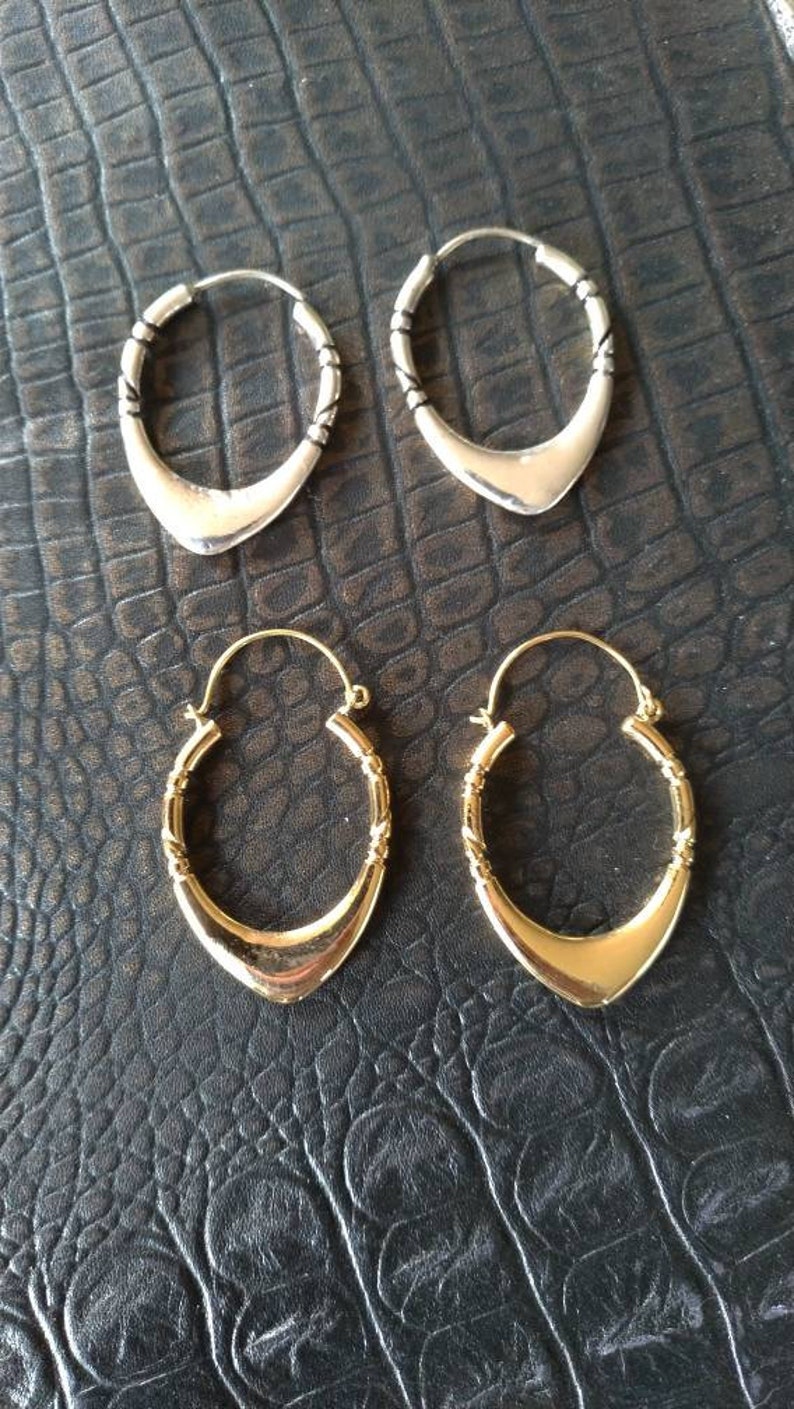 May include: Two pairs of hoop earrings, one pair is silver and the other is gold. Both pairs have a unique, slightly pointed, teardrop shape.