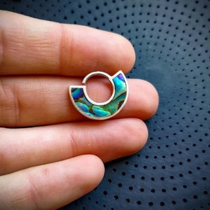 May include: A silver hoop earring with a half-circle of iridescent abalone shell inlay. The shell has shades of blue, green, and purple.