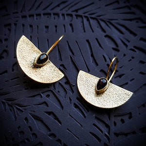 Peut inclure: Une paire de boucles d'oreilles en or avec des accents de pierres précieuses noires. Les boucles d'oreilles sont en forme de demi-cercles et ont une surface texturée.