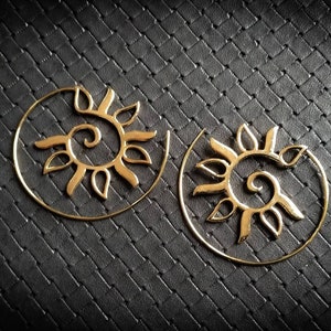 Peut inclure: Une paire de boucles d'oreilles créoles dorées avec un motif soleil et spirale. Les boucles d'oreilles sont en métal et ont une forme circulaire.
