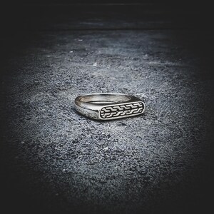 May include: A silver ring with a rectangular face featuring a detailed, repeating pattern. The ring has a polished finish and a classic, understated design. The ring is likely made of sterling silver or a similar metal.