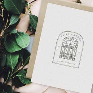May include: A black and white illustration of a decorative iron gate with the text "Fairy Garden Flower Boutique" below it.