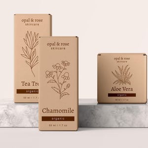 K&ouml;nnte beinhalten: Drei braune Pappkartons mit Produktetiketten. Die Kartons sind mit "Tea Tree", "Chamomile" und "Aloe Vera" beschriftet. Jede Schachtel zeigt eine Strichzeichnung einer Pflanze und den Text "opal & rose skincare" und "organic".