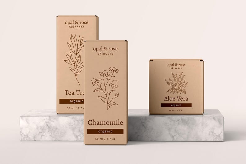 K&ouml;nnte beinhalten: Drei braune Pappkartons mit Produktetiketten. Die Kartons sind mit "Tea Tree", "Chamomile" und "Aloe Vera" beschriftet. Jede Schachtel zeigt eine Strichzeichnung einer Pflanze und den Text "opal & rose skincare" und "organic".