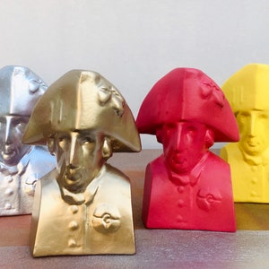 May include: A set of ten bust sculptures of a man wearing a tri-corner hat. The busts are painted in various colors, including white, black, silver, gold, red, yellow, blue, and green.