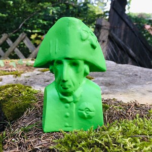 May include: A green bust sculpture of a person wearing a hat. The sculpture is made of a smooth material and has a simple design.