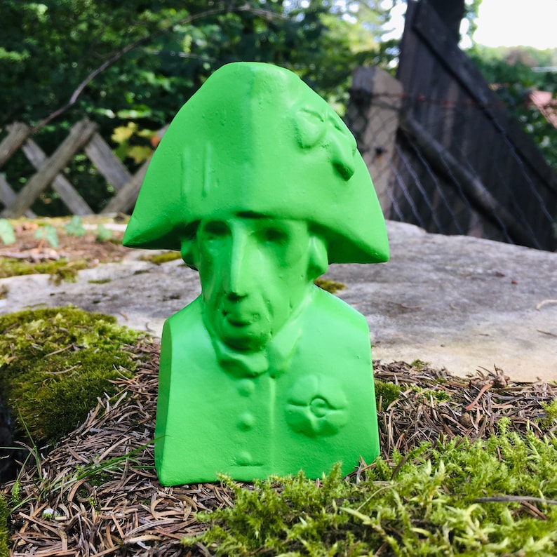 May include: A green bust sculpture of a person wearing a hat. The sculpture is made of a smooth material and has a simple design.