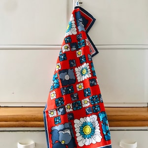 May include: A red tea towel with a blue and white floral pattern. The towel is hanging on a white cabinet door.