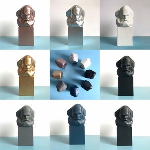 May include: A selection of Karl Marx bust sculptures in diverse colours, including metallic bronze, silver, and gold, alongside matte white, black, and grey. The busts are mounted on rectangular plinths, with additional smaller, irregularly shaped sculptures.