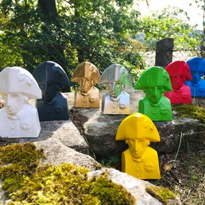 May include: A collection of eight bust sculptures of a man wearing a bicorne hat. The sculptures are painted in various colors, including white, black, gold, silver, green, yellow, red, and blue.
