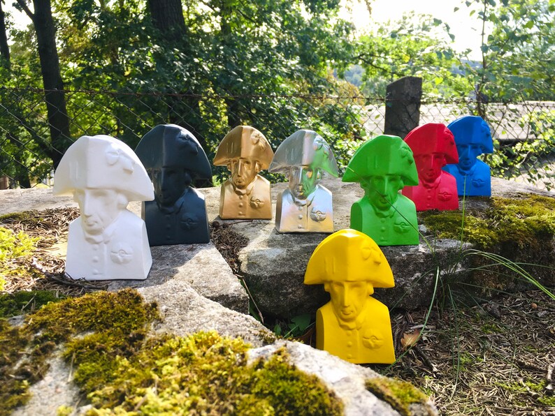 May include: A collection of eight bust sculptures of a man wearing a bicorne hat. The sculptures are painted in various colors, including white, black, gold, silver, green, yellow, red, and blue.