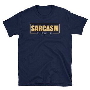 May include: A navy blue t-shirt with a gold rectangle that says "SARCASM - IT'S HOW I HUG"