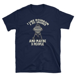 Puede incluir: Una camiseta azul marino con el texto "Me gusta el bourbon y mi ahumador y quiz&aacute;s 3 personas" en blanco. Una imagen de dibujos animados de un ahumador est&aacute; en el centro del texto.