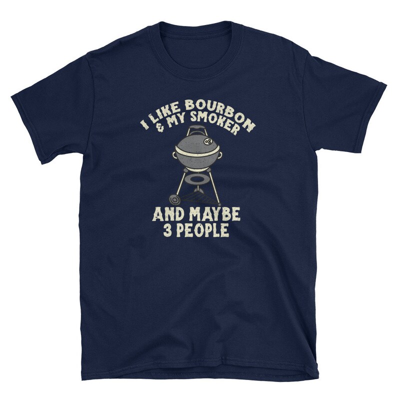 Puede incluir: Una camiseta azul marino con el texto "Me gusta el bourbon y mi ahumador y quiz&aacute;s 3 personas" en blanco. Una imagen de dibujos animados de un ahumador est&aacute; en el centro del texto.