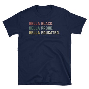 May include: A navy blue t-shirt with the phrases "HELLA BLACK. HELLA PROUD. HELLA EDUCATED." printed in a retro font. The text is in red, green, and tan colors. The shirt is a short-sleeved crew neck.