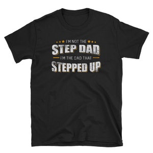 Op de afbeelding: Zwart T-shirt met witte tekst die luidt "Ik ben niet de stiefvader - Ik ben de vader die een stap vooruit heeft gezet" met gouden sterren boven de tekst.