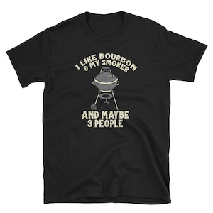 Puede incluir: Camiseta negra con texto blanco que dice "Me gusta el bourbon y mi ahumador y quiz&aacute;s 3 personas". Una ilustraci&oacute;n en blanco y negro de una parrilla de ahumado est&aacute; en el centro del texto.