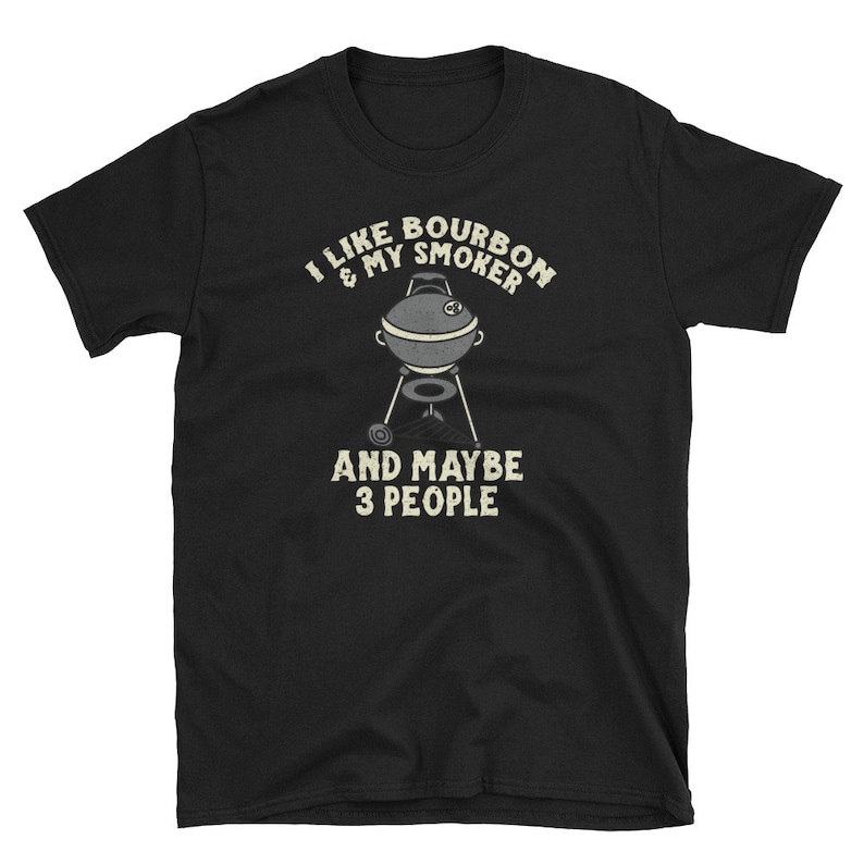 Puede incluir: Camiseta negra con texto blanco que dice "Me gusta el bourbon y mi ahumador y quiz&aacute;s 3 personas". Una ilustraci&oacute;n en blanco y negro de una parrilla de ahumado est&aacute; en el centro del texto.