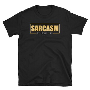 May include: Black t-shirt with a gold rectangle that says "SARCASM - IT'S HOW I HUG"