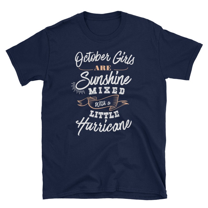 May include: Navy blue t-shirt with the text "October Girls are Sunshine Mixed with a Little Hurricane" in white and peach-colored script. The shirt has a crew neck and short sleeves.