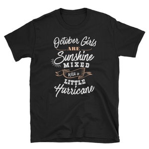 May include: Black t-shirt with the text "October Girls are Sunshine Mixed with a Little Hurricane" in white and peach lettering. The shirt is a short-sleeved crew neck.