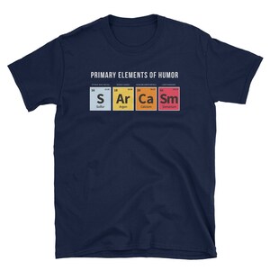 May include: A navy blue t-shirt with a white graphic of the periodic table elements, spelling out "S Ar Ca Sm" for "Sarcasm". The text "PRIMARY ELEMENTS OF HUMOR" is above the graphic.
