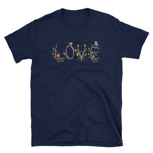 Pu&ograve; includere: Maglietta blu navy con una grafica della parola "LOVE" formata da rami con uccelli appollaiati su di essi. Gli uccelli sono rossi, gialli, blu e verdi.