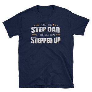 Op de afbeelding: Donkerblauw T-shirt met een witte, verweerde afbeelding met de tekst "Ik ben niet de stiefvader, ik ben de vader die een stap vooruit heeft gezet".