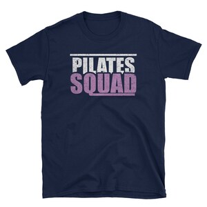 May include: Navy blue t-shirt with a white and pink distressed graphic that says "PILATES SQUAD".