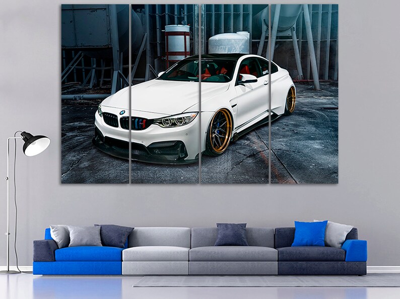 K&ouml;nnte beinhalten: Ein wei&szlig;er BMW M4 Sportwagen mit schwarzen Akzenten und goldenen Felgen steht in einer Garage. Das Auto ist zur Kamera gerichtet und die Front des Autos ist scharf.