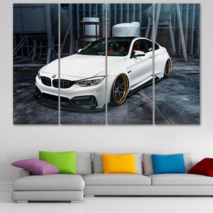 K&ouml;nnte beinhalten: Ein wei&szlig;er BMW M4 Sportwagen mit schwarzen Akzenten und goldenen Felgen steht in einer industriellen Umgebung. Das Auto ist in vier Paneele aufgeteilt, wodurch ein mehrteiliges Kunstwerk entsteht.