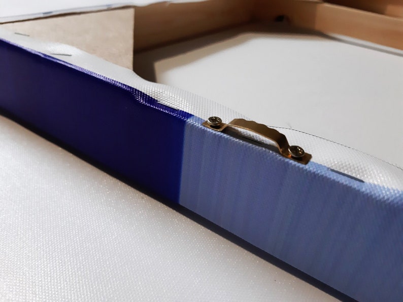 K&ouml;nnte beinhalten: Nahaufnahme eines blauen und wei&szlig;en Leinwandgem&auml;ldes mit einem goldenen Metall-Aufh&auml;nger an der R&uuml;ckseite.