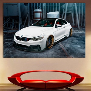 K&ouml;nnte beinhalten: Ein wei&szlig;er BMW M4 Sportwagen, der in einer Garage steht. Das Auto hat schwarze Akzente und goldene Felgen.