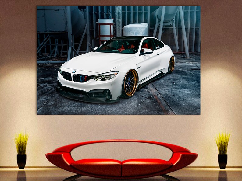 K&ouml;nnte beinhalten: Ein wei&szlig;er BMW M4 Sportwagen, der in einer Garage steht. Das Auto hat schwarze Akzente und goldene Felgen.