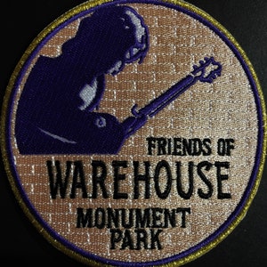 May include: A purple embroidered patch with a silhouette of a person playing a guitar. The text "FRIENDS OF WAREHOUSE MONUMENT PARK" is embroidered in black on a beige background.