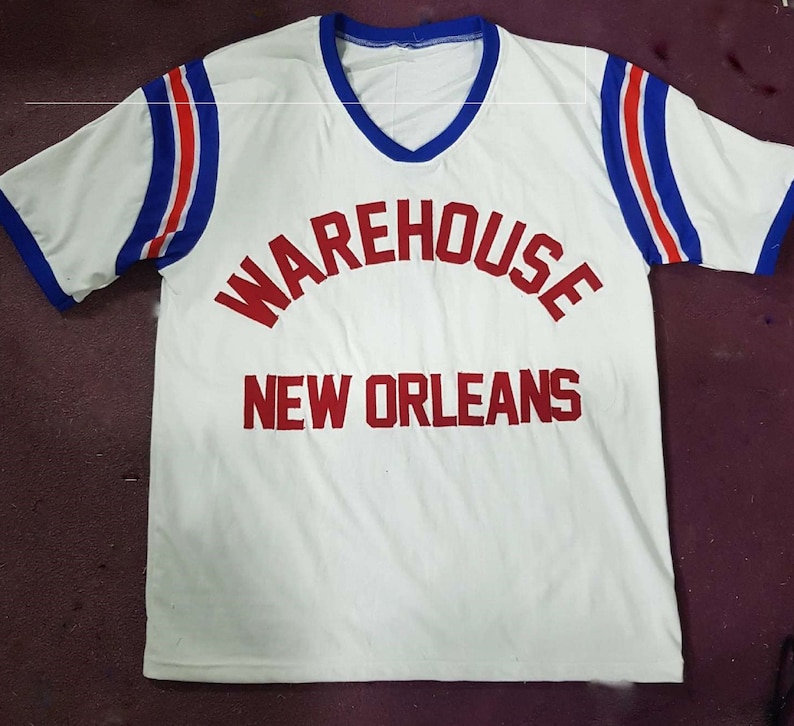 May include: White short-sleeved t-shirt with red and blue striped sleeves. The shirt has the text "WAREHOUSE NEW ORLEANS" printed in red.