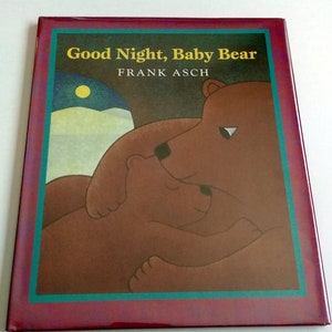 May include: A red hardcover book with a teal border. The cover features a brown bear and a baby bear cuddling. The title "Good Night, Baby Bear" is printed in yellow letters. The author "FRANK ASCH" is printed in white letters.